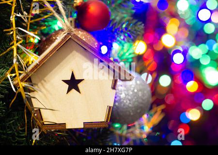 Maison de Noël en bois sur l'arbre de Noël sur le fond lumineux coloré.Belles décorations de Noël.Jouets du nouvel an frais et lumineux Banque D'Images