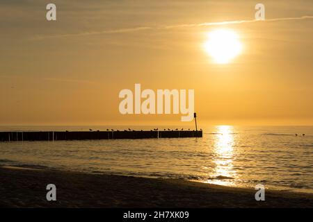 Le coucher de soleil sur la mer Baltique arrive, et au loin les silhouettes de brise-lames sont vus, le ciel a déjà commencé à prendre un col du soir Banque D'Images