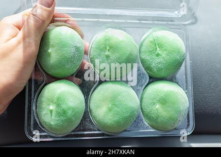 Macro gros plan de la main tenant stockeacheté glace surgelé gâteau de riz mochi japonais dessert avec thé vert saveur matcha montrant la texture Banque D'Images