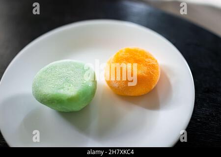 Macro-gros plan d'une assiette blanche avec deux gâteaux de riz mochi congelés à la crème glacée, dessert japonais avec saveur de matcha de thé vert et mangue montrant la texture Banque D'Images