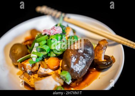 Plat traditionnel japonais macro de gros plan avec champignons, tofu et oignons verts de baguettes d'assiette dans la maison ryokan restaurant hôtel avec bac noir Banque D'Images