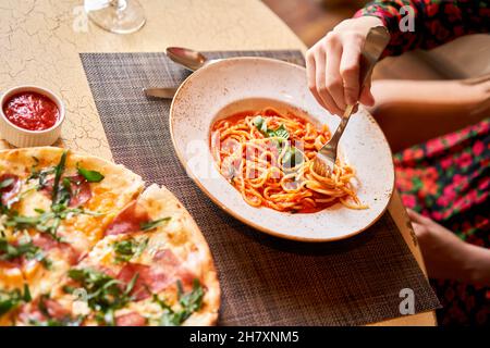 La femme mange des pâtes italiennes avec de la tomate, de la viande.Gros plan spaghetti bolognaise enroulez-la autour d'une fourchette à l'aide d'une cuillère.Parmesan. Banque D'Images