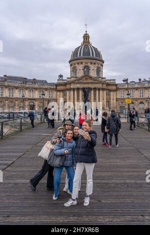 Paris, France - 11 13 2021: Vue d'un groupe de jeunes touristes souriants prenant le selfie sur le Pont des Arts avec l'Institut de France derrière Banque D'Images