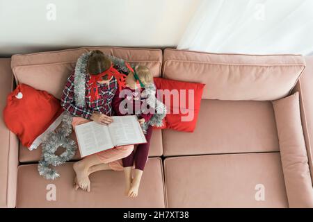 Mère avec fille portant des pyjamas et des cornes de cerf de bois pendant la lecture d'un livre.Jeune femme embrassant sa petite fille pendant Banque D'Images