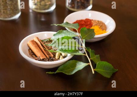 Mélange d'épices asiatiques utilisé pour faire du curry sur une table en bois avec des feuilles de curry fraîches comme garniture Banque D'Images