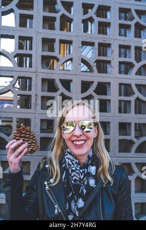 Jolie femme blonde aux cheveux tient une grande pomme de pin contre géométrique treillis Banque D'Images