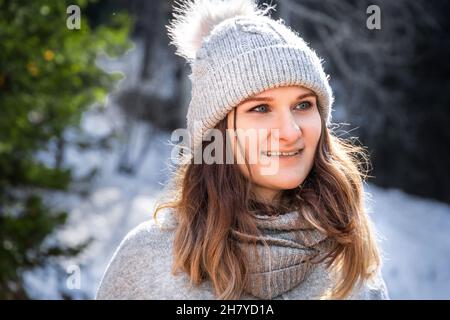 Portrait d'hiver de blanc blanc jeune femme souriante heureuse en chandail gris et chapeau pompon extérieur. Banque D'Images