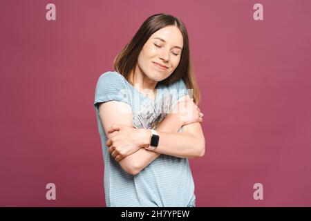 Photo d'une jeune femme heureuse isolée sur fond rose embrassant l'argent, rêvant de quelque chose d'agréable Banque D'Images