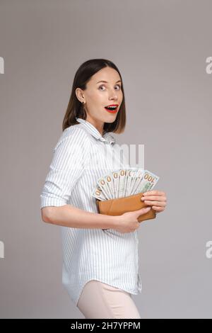 Photo d'une jeune femme excitée surprise isolée sur fond gris tenant de l'argent dans un portefeuille Banque D'Images