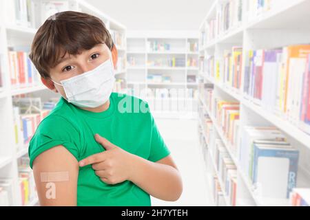 Enfant pointant sur le plâtre après la vaccination du coronavirus à l'école portant un masque facial contre le virus Corona COVID-19 Covid copyspace copy space latin Banque D'Images