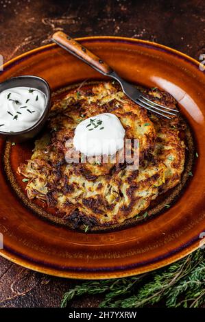 Crêpes de pommes de terre ou beignets à la sauce crème dans une assiette rustique. Arrière-plan sombre. Vue de dessus Banque D'Images