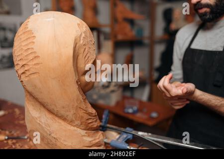Crop anonyme homme menuiserie dans un tablier debout près de sculpture en bois sculpté sur la table avec l'équipement professionnel tout en travaillant dans la menuiserie Banque D'Images
