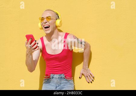 Jeune personne non binaire riant et s'amusant tout en écoutant de la musique avec un casque et un téléphone portable. Banque D'Images