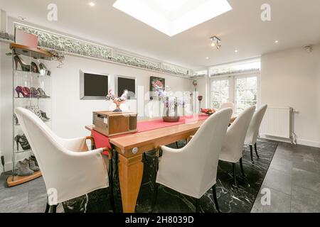 Salle de conférence moderne éclairée avec table en bois décorée et fauteuils confortables près de la fenêtre et chaussures dans un coffret Banque D'Images