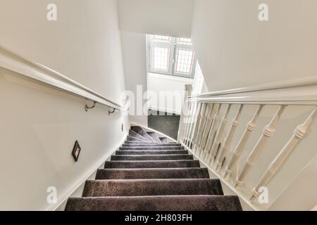 De dessus de long escalier avec des rampes blanches entre les murs menant à un couloir étroit avec fenêtre de l'appartement moderne lumineux Banque D'Images