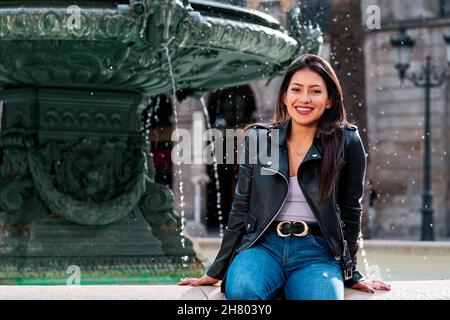 Femme souriant assis sur une fontaine à l'extérieur. Banque D'Images