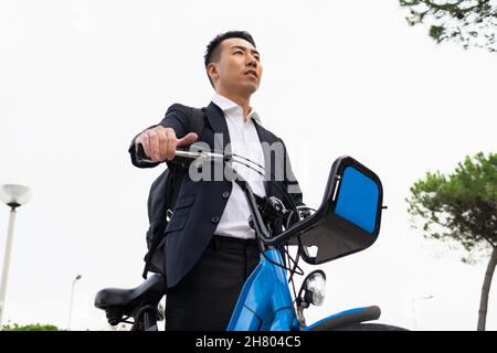 D'en-dessous sérieux homme d'affaires asiatique dans la marche élégante avec vélo dans la ville Banque D'Images