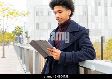 Positif Africain américain avec des cheveux bouclés vêtus de manteau sur tablette tout en souriant dans la rue Banque D'Images