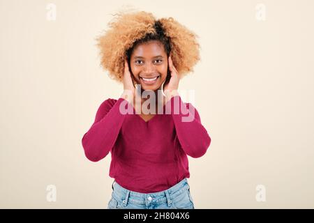 Jeune femme aux cheveux bouclés souriant tout en se tenant debout sur un fond isolé. Banque D'Images
