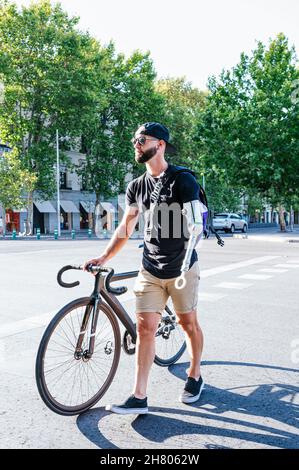 Hipster mâle avec prothèse de bras marchant avec un vélo sur la voie de la chaussée dans la ville Banque D'Images