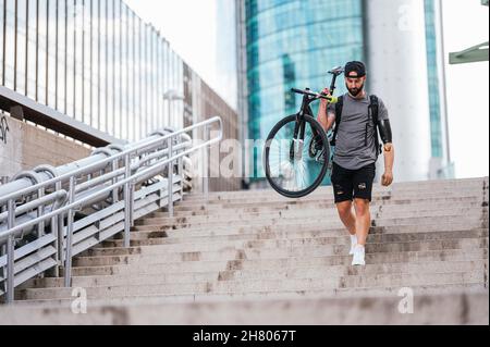 Boxer mâle avec prothèse de bras tenant un vélo et marchant sur des marches en pierre dans la ville Banque D'Images