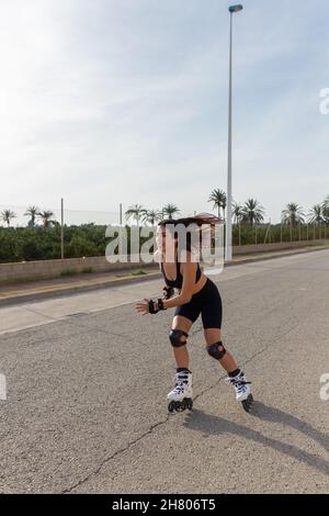 Corps complet de la femme en forme d'activewear avec les cheveux volants de patinage sur les lames de rouleau et d'écouter de la musique dans les écouteurs TWS Banque D'Images