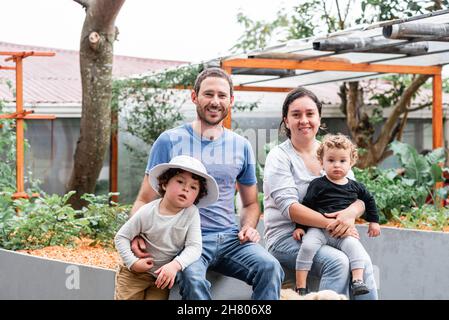 Parents heureux avec de jolis fils assis sur le lit de jardin avec Golden Retriever chiot en campagne regardant l'appareil photo Banque D'Images