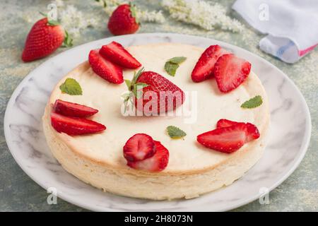 Cheesecake rond savoureux décoré de fraises mûres et de feuilles de menthe verte servies sur une assiette à table dans une cuisine légère Banque D'Images