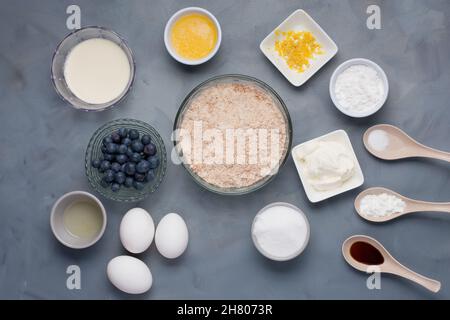 Vue de dessus de différents ingrédients dont le lait beurre fondu près des bols de zeste de citron sucre sel de sucre près de la crème aigre soda huile et des oeufs de bleuets Banque D'Images