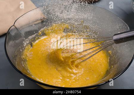 Farines versées dans un bol en verre avec du jaune d'œuf fouetté brut et fouetter placées sur une table dans la cuisine pendant la cuisson Banque D'Images