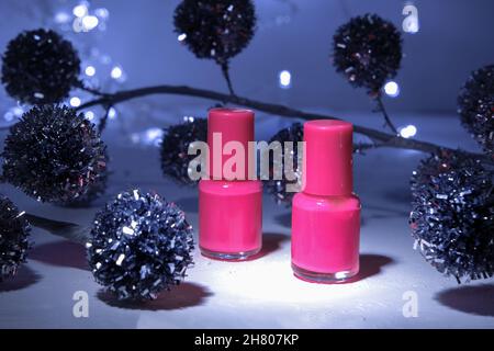 Maquette de Noël créative de bouteille cosmétique isolée avec vernis à ongles rose sur fond de Noël avec lumières et décorations de Noël, ombre dure Banque D'Images