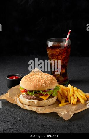 Hamburger frais et savoureux, frites et boisson non alcoolisée sur fond sombre Banque D'Images