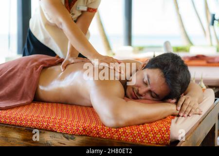 Homme asiatique au spa de la plage se faire masser à l'huile près de la plage et se faire plaisir en Thaïlande.Spa, complexe, beauté et concept de santé. Banque D'Images