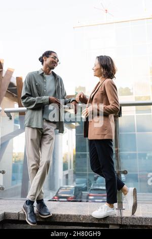 vue sur toute la longueur d'un couple interracial dans des vêtements tendance qui parlent sur le balcon Banque D'Images