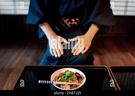 Restaurant traditionnel japonais ryokan avec plateau de table en bois laqué noir et plat de cuisine fermé de champignons et tofu et homme en kimono ou yuk Banque D'Images