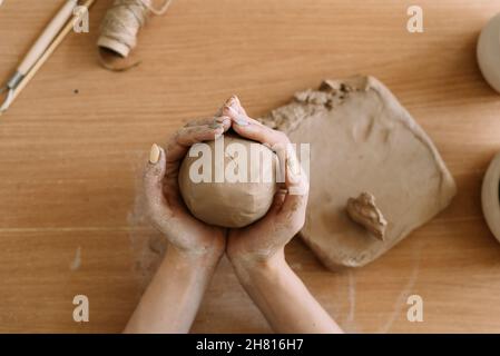 potter travaille avec l'argile, gros plan vue de dessus les mains femelles tiennent un morceau d'argile humide dans leurs mains.Le potier crée un produit. Banque D'Images