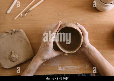 atelier de poterie concept d'art en argile. gros plan sur les mains d'un jeune céramiste avec un pot en argile non cuit. mains artisanales tiennent une coupe en argile et un Banque D'Images