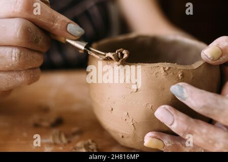 les mains d'un potier en argile sculpte un modèle sur le bol.Vue latérale.Céramique et argile pour la créativité dans l'atelier. Banque D'Images