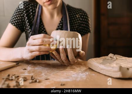 Woman potter travaille avec l'argile dans son atelier à la maison, les mains du maître gros plan, les genoux et sculpte l'argile avant le travail, la focalisation sélective. Hobby créatif Banque D'Images