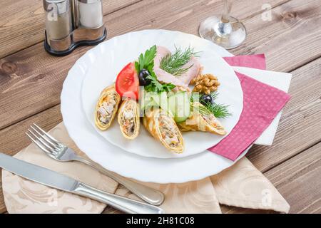 Crêpes farcies au jambon décoré d'herbes sur une assiette blanche sur un fond en bois sombre Banque D'Images