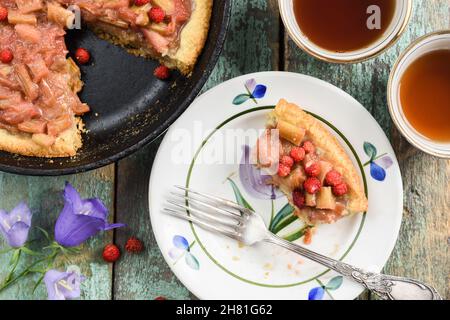 Tarte rustiques à la rhubarbe avec fraises forestières fraîches cuites dans un poêlon en fonte servi avec du thé noir et des fourchettes millésimes, vue sur le dessus Banque D'Images