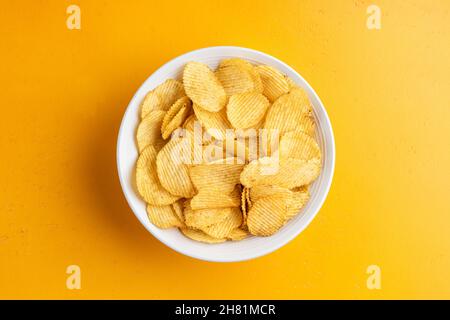 Chips de pommes de terre ou chips de pommes de terre à mousselures épicées dans un bol isolé sur fond jaune, vue du dessus espace de copie pour le dessin ou le texte Banque D'Images