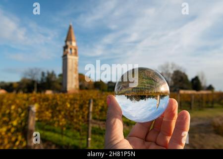 Campanile di Sant Angelo sur l'île de Mazzorbo près de Burano (Venise, Italie) par une journée ensoleillée en automne, feuilles colorées, main tenant une boule de verre Banque D'Images