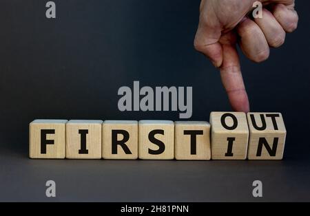 Premier dans premier sorti.L'homme d'affaires tourne des cubes en bois et change de mots d'abord en premier.Belle table grise, fond gris.Entreprise et Banque D'Images