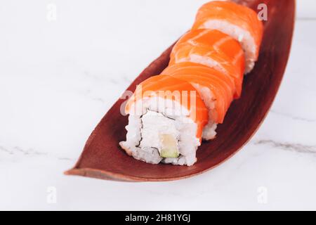 Ensemble de sushis futomaki traditionnels avec saumon servi sur des feuilles séchées sur fond de table en marbre blanc avec espace pour les copies. Livraison de nourriture asiatique, sushi Banque D'Images