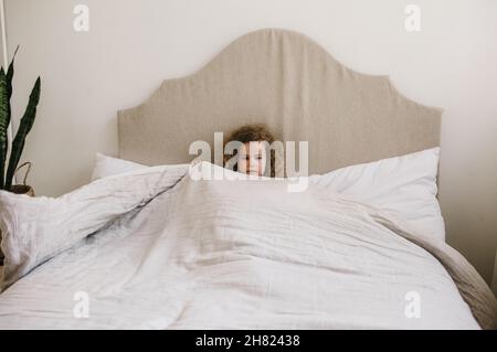 Jolie petite fille aux cheveux bouclés couchée dans un lit sur un oreiller blanc.Le concept de l'enfance. Banque D'Images