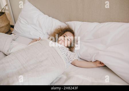 Jolie petite fille aux cheveux bouclés couchée dans un lit sur un oreiller blanc.Le concept de l'enfance. Banque D'Images