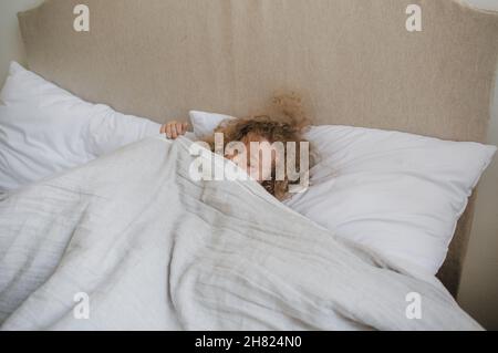 Jolie petite fille aux cheveux bouclés couchée dans un lit sur un oreiller blanc.Le concept de l'enfance. Banque D'Images