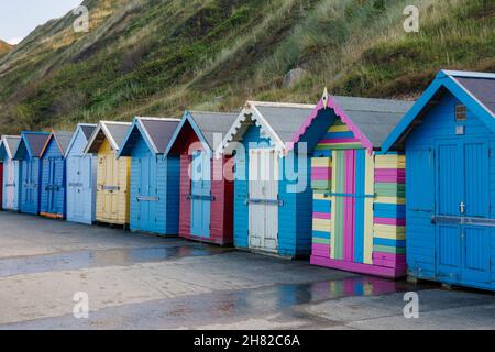 Une rangée de cabanes de plage colorées avec volets sur la promenade du front de mer sous les falaises de Sheringham, sur la côte nord de Norfolk, East Anglia, Angleterre Banque D'Images