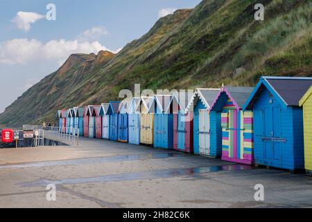 Une rangée de cabanes de plage colorées avec volets sur la promenade du front de mer sous les falaises de Sheringham, sur la côte nord de Norfolk, East Anglia, Angleterre Banque D'Images